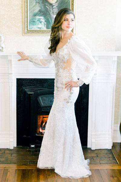 Lauren posing by the fireplace in her custom wedding gown from Angela Kim Couture