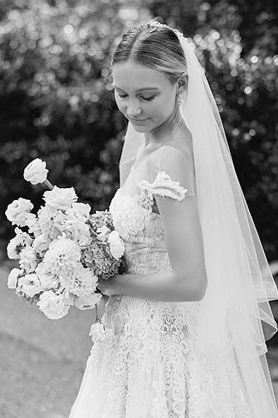 Natalie in a lace wedding gown posing for wedding photos with a bouquet.